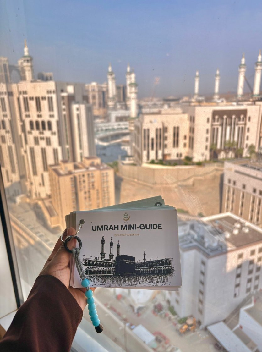 Umrah Mini-Guide booklet held up against the Makkah skyline
