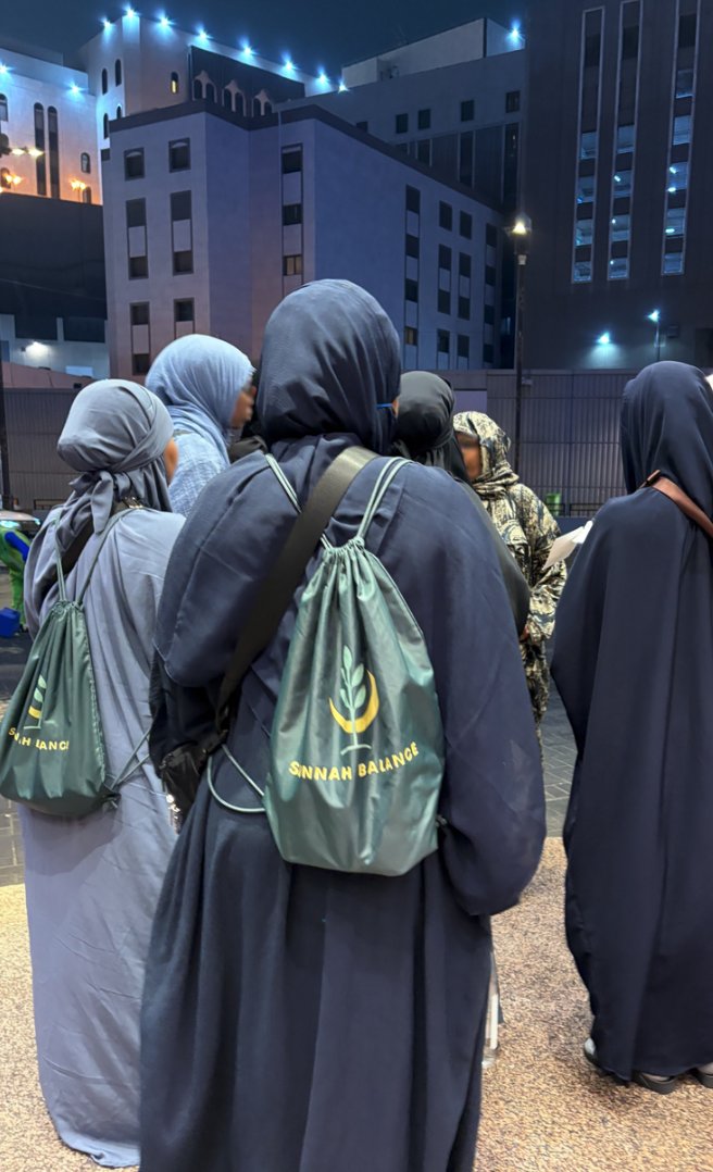 Group standing outdoors at night in Makkah, in ihram, wearing Sunnah Balance bags