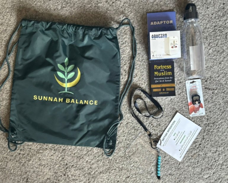 The full Sunnah Balance Umrah kit laid out: drawstring bag, Fortress of the Muslim, travel adaptor, water bottle, tasbih and niyyah card
