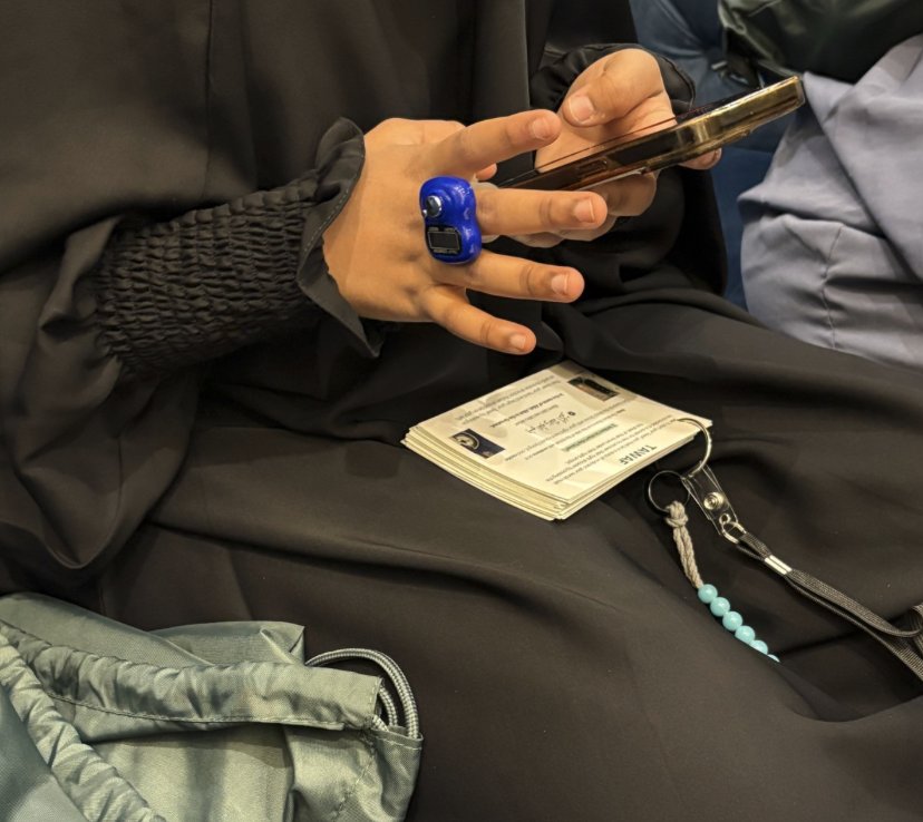 Hand wearing a tasbih ring counter while holding the Umrah mini-guide